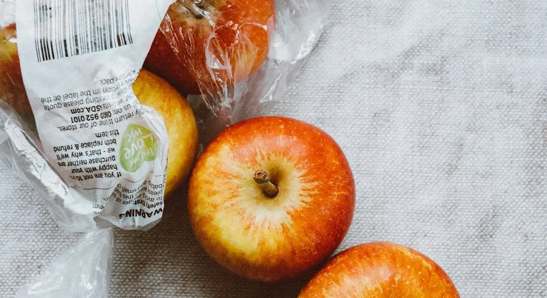 Two red apples on a light gray fabric surface with a plastic bag visible in the background.