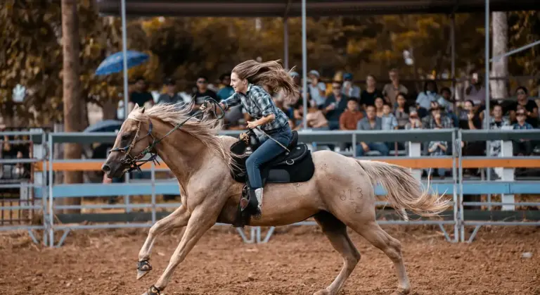 A rider on a galloping horse in a dusty arena with spectators in the background.