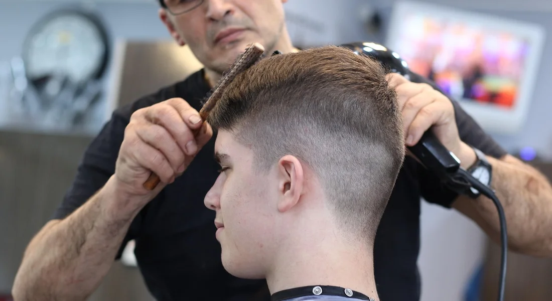 Barber trimming a client's hair with clippers, emphasizing the need for routine maintenance of cutting tools