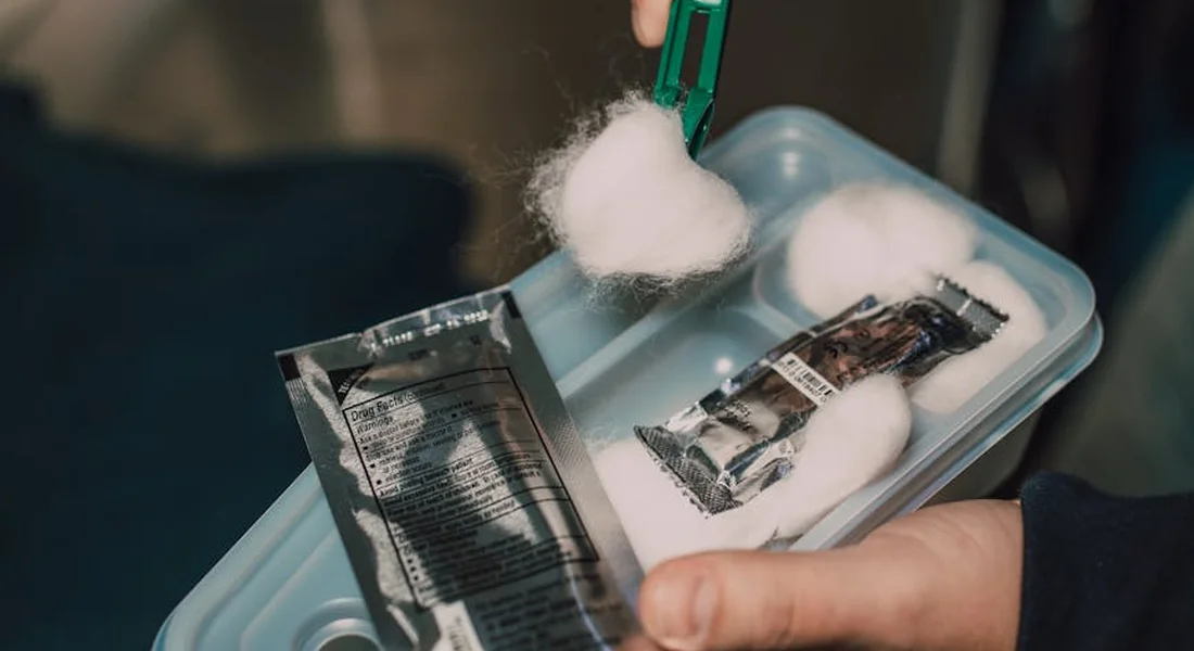 Hands arranging a plastic first aid kit with cotton balls and small packets for quick access.