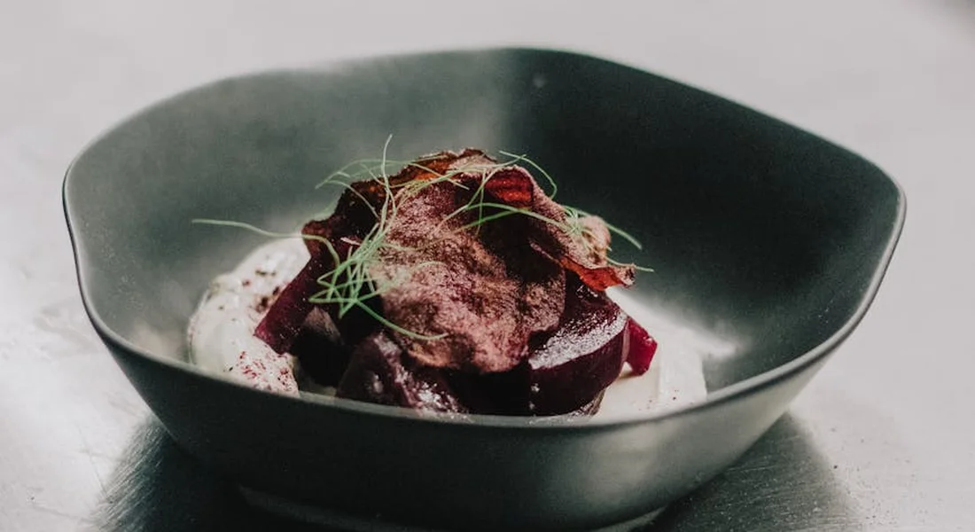 A dark bowl filled with sliced red beets and greens on a reflective surface.