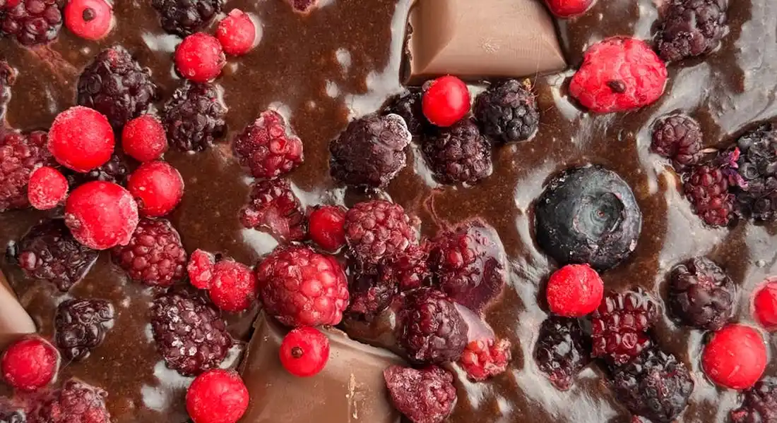 Close-up of melted chocolate with red berries and blackberries on a surface, illustrating unsafe snacks for horses.