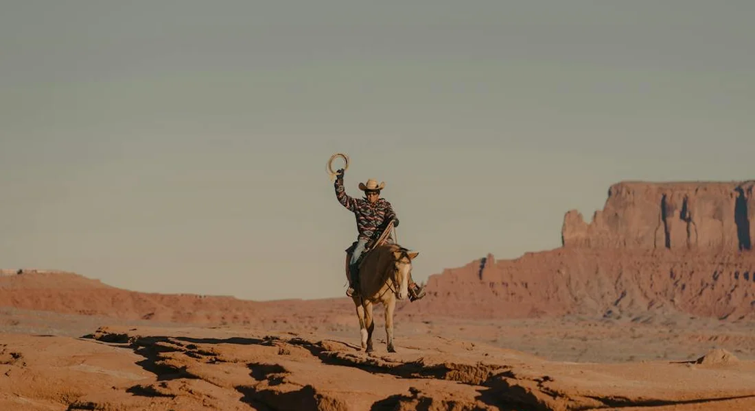 Horse and rider on a desert trail with red rock formations at sunset