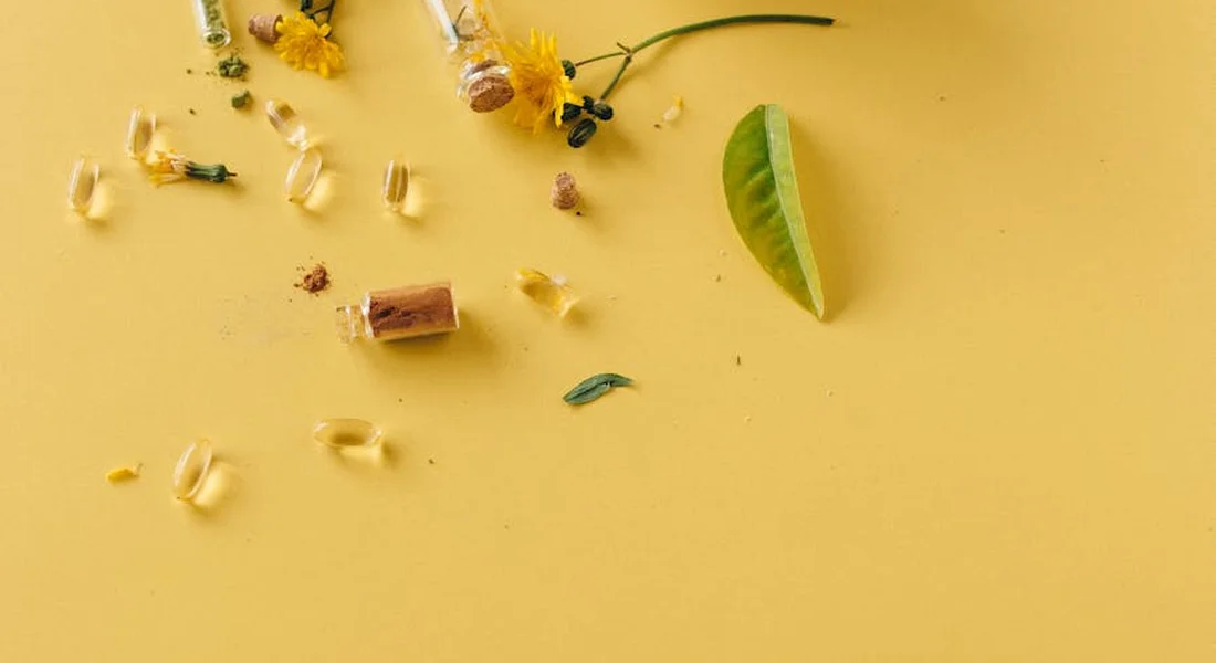 Assorted horse supplement capsules and tablets scattered on a bright yellow surface, with a small green leaf and yellow flowers.
