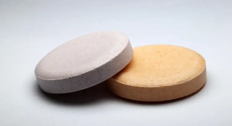 Two round tablets, one gray and one tan, resting on a pale surface