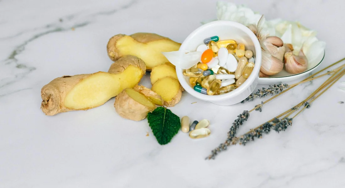 Ginger root, garlic, lavender sprigs, and a bowl of assorted capsules on a marble surface, illustrating natural supplements for horses.