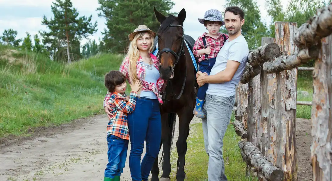 Family posing with a horse outdoors beside a wooden fence