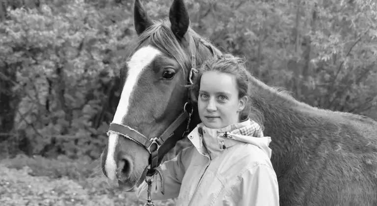 Person standing next to a horse outdoors in black and white, wearing a light jacket