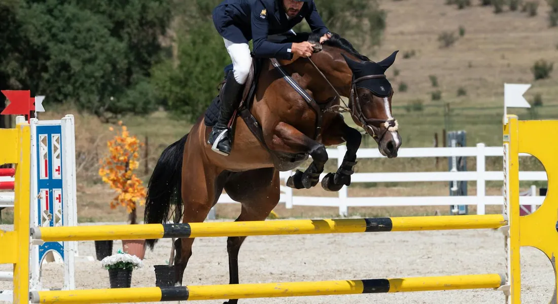 A rider and horse jumping over a bright yellow and black obstacle in an outdoor riding arena.