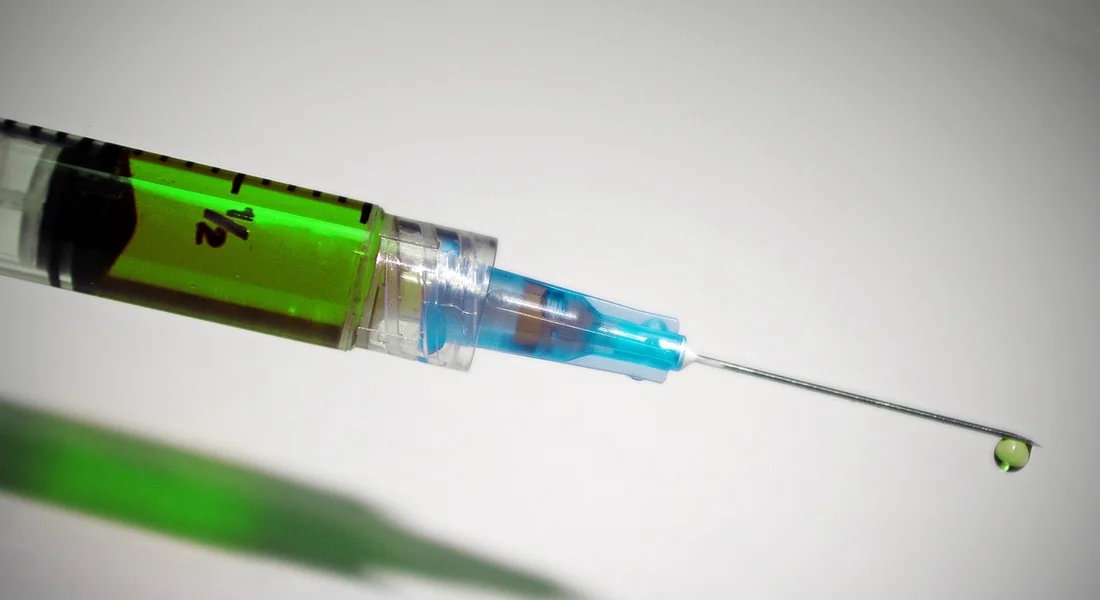 Close-up of a syringe with green liquid and a needle, symbolizing preventive medications for a horse's hoof and skin care.