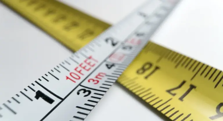Close-up of yellow and white measuring tapes overlapped, showing inch and foot markings