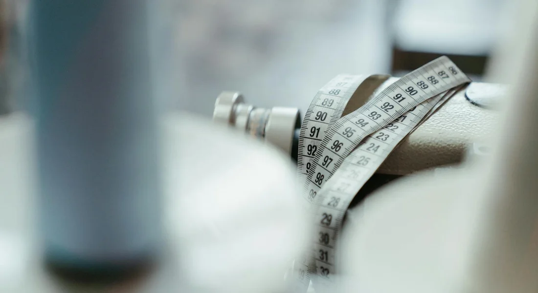 Close-up of a soft measuring tape wrapped around a horse's girth for weight estimation, with blurred equipment in the background