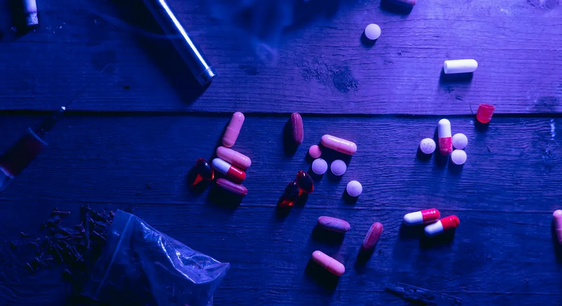 Pills and capsules scattered on a dark wooden surface under blue lighting, symbolizing horse deworming medications.