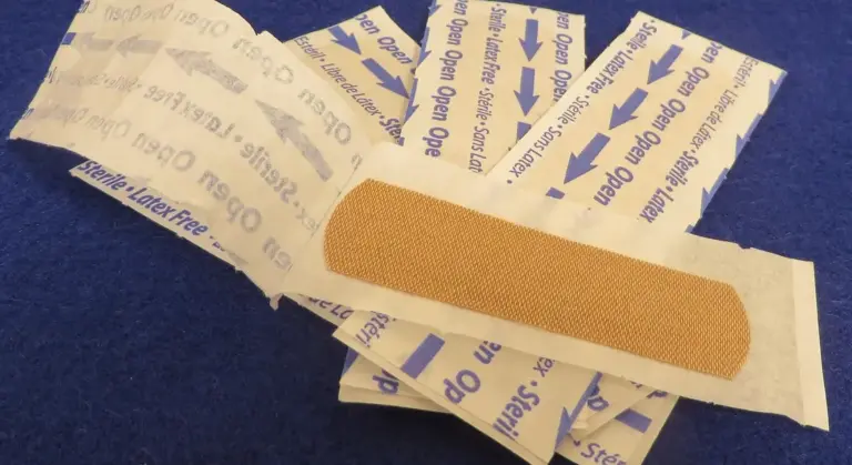 A close-up of an adhesive bandage placed on a blue surface, with scattered sterile bandage wrappers around it.