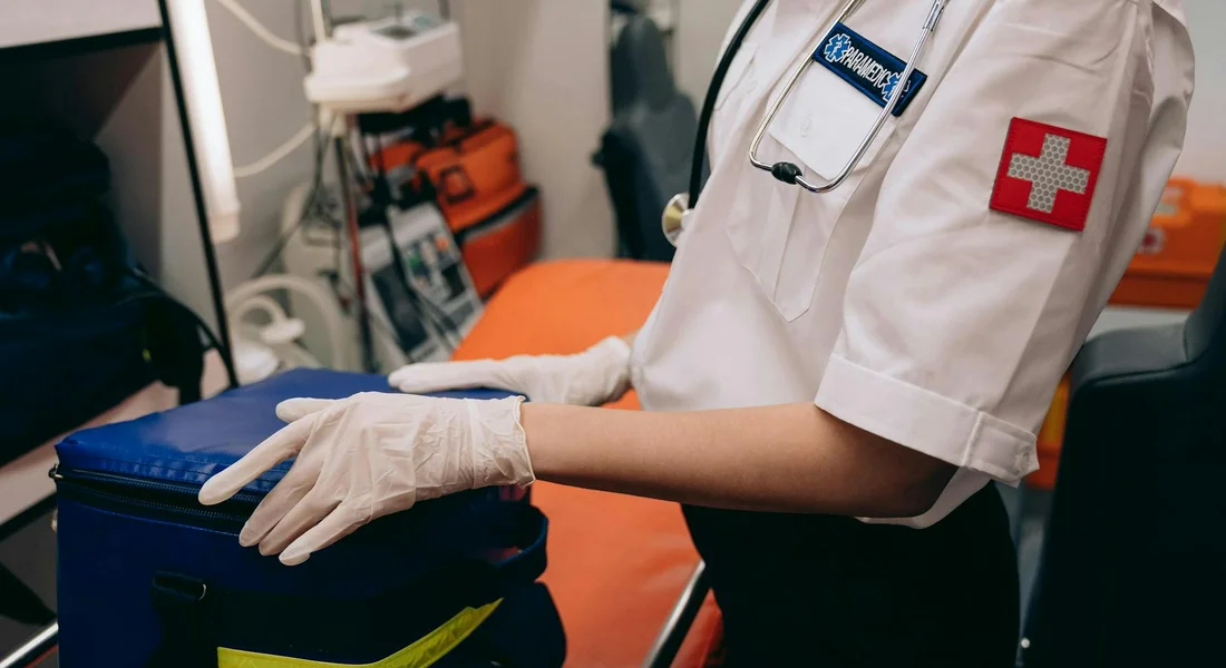 Veterinary professional in a white uniform and gloves opening a blue first aid kit.