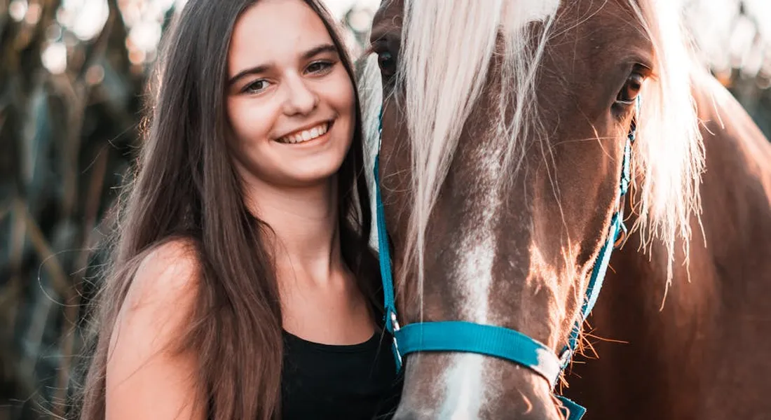 A smiling young woman stands beside a horse with a blue halter, illustrating everyday horse care.