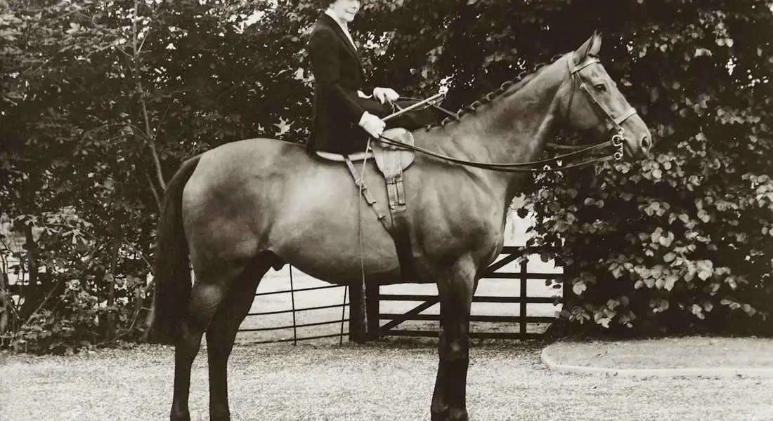 Vintage black-and-white photograph of a person mounted on a horse in an outdoor enclosure.