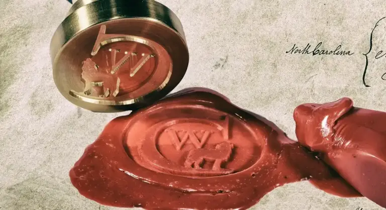 Close-up of a red wax seal stamped with a circular emblem and a metal seal, resting on parchment.