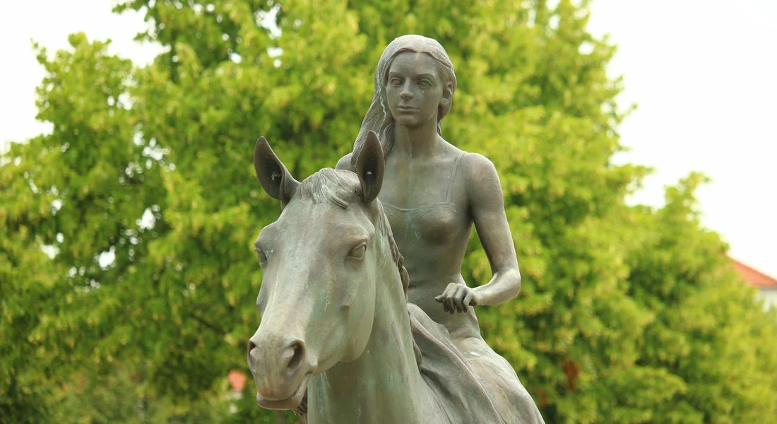 Bronze statue of a rider on a horse set in a green park.
