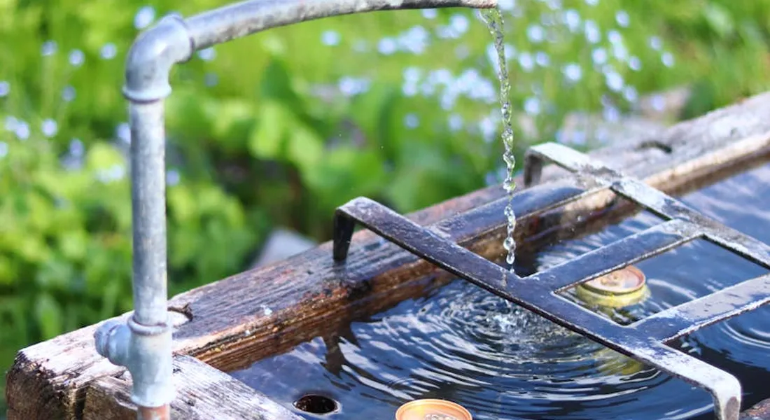 Close-up of a metal spout filling a wooden horse trough with clear, rippling water