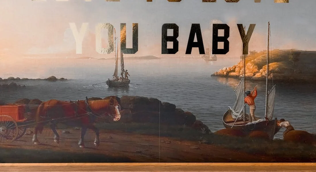 Painting-style coastal scene with two horses pulling a carriage along rocky shoreline, with a small sailboat in the water; large weathered letters across the top spell 'YOU BABY'.
