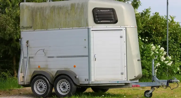 A two-axle enclosed trailer with a white and gray exterior parked on grass, featuring a hitch and small side door.