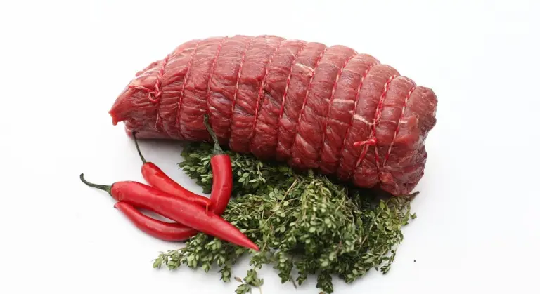 Raw beef roast with herbs and red chili peppers on a white background