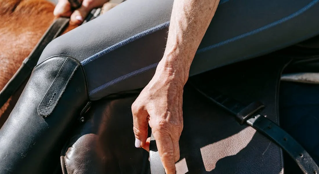 Close-up of a rider's hand adjusting a saddle on a horse, illustrating tack fitting and routine care.