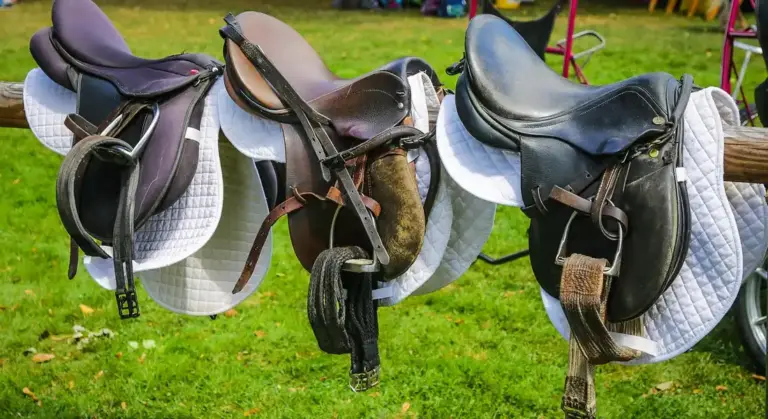 Three Western saddles with white saddle pads hanging on a rack outdoors