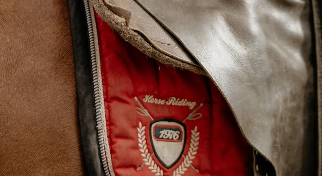 Close-up of a riding saddle jacket lining with a crest that includes the year 1976 and laurel wreaths.