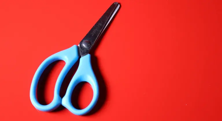 Blue-handled scissors on a bright red background