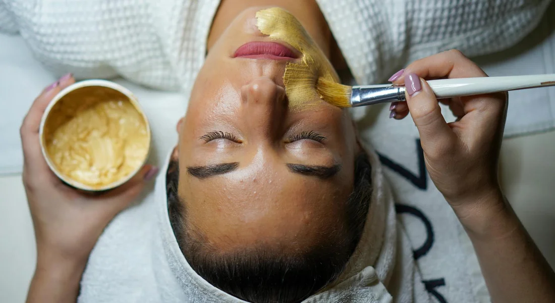 A woman relaxing with a facial mask as a technician applies product with a brush.