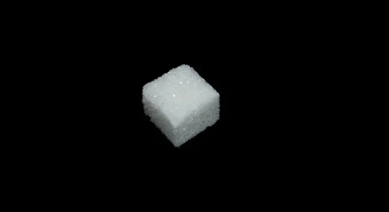 Close-up of a single white sugar cube on a black background