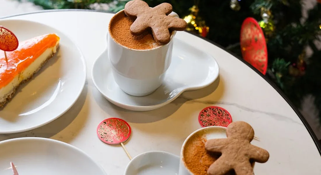Gingerbread cookies and a cup of cappuccino on a marble table, with a Christmas tree blurred in the background.