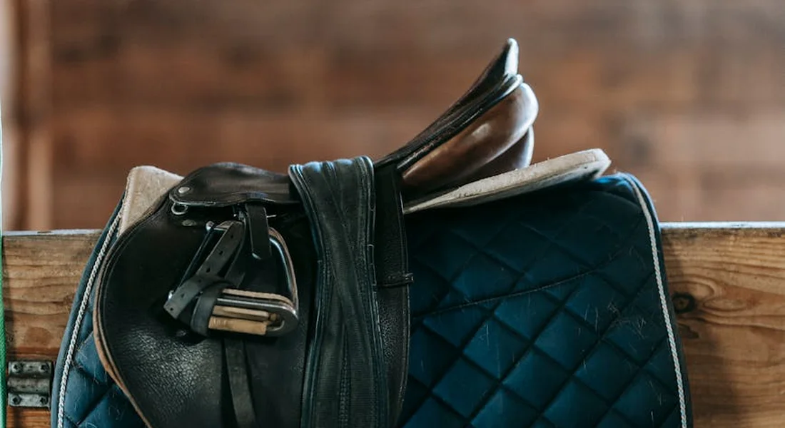 Close-up of a leather saddle with a blue quilted saddle pad resting on a wooden rack