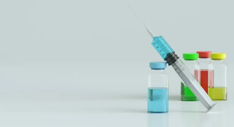A syringe with a needle and several vaccine vials on a clean surface, ready for veterinary injection.