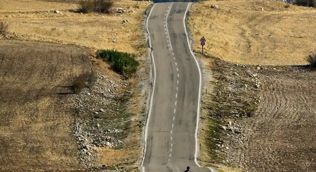 A narrow winding country road through dry, grassy hills, illustrating lifestyle considerations when owning a small horse breed.